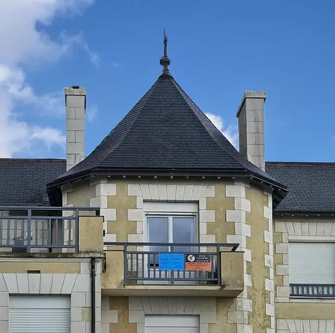 Façade d'immeuble résidentiel avec tour conique à toiture ardoise et finition pierres d'angle