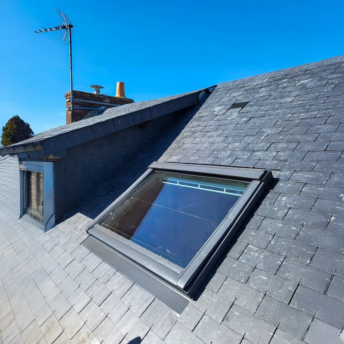 Toiture d'ardoise avec fenêtre de toit ouverte intégrée dans les combles d'une maison traditionnelle