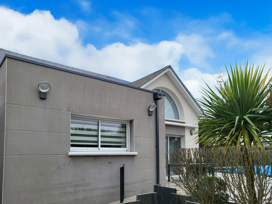 Façade extérieure d'une maison moderne avec murs en crépi beige, toiture en ardoise grise