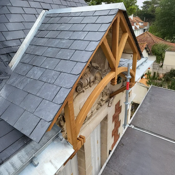 Vue aérienne d'une toiture résidentielle complexe avec bardeaux d'asphalte gris, présentant plusieurs sections à pignons et lucarnes triangulaires éclairées