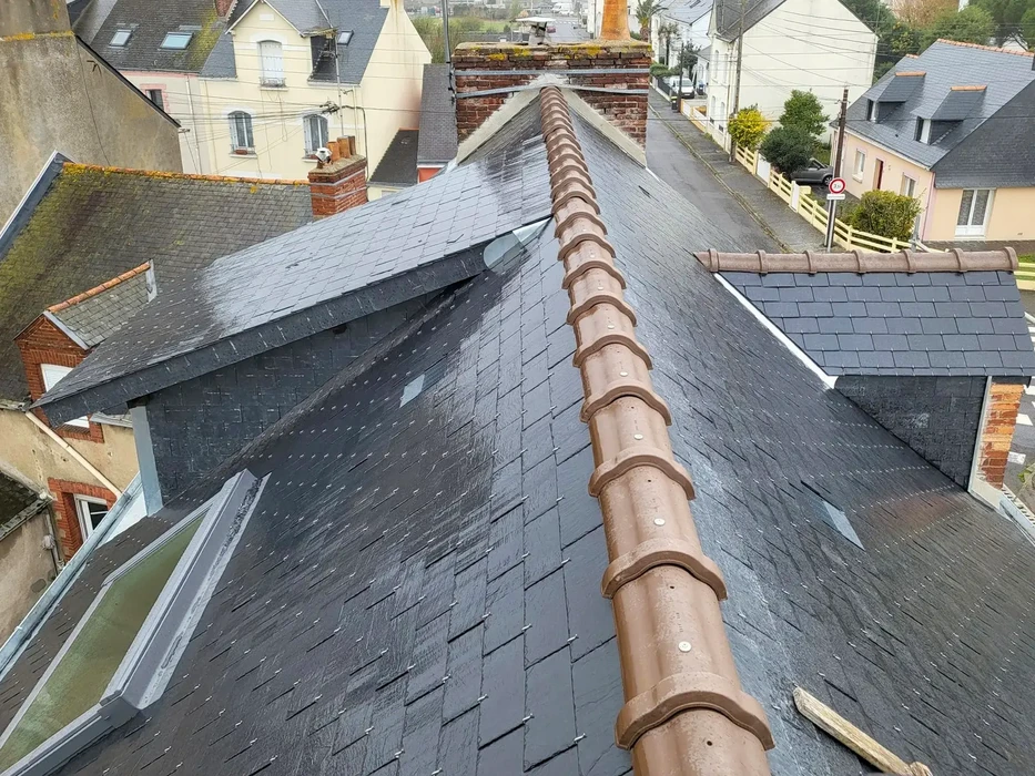 Vue ext&eacute;rieure d'une toiture en tuiles grises sous ciel bleu nuageux avec chemin&eacute;e m&eacute;tallique visible